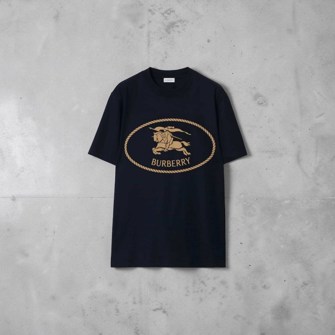 Close-up of the gold Burberry Equestrian Knight Design (EKD) logo on a navy t-shirt.