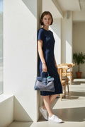 Model wearing navy blue silk dress carrying a Goyard Saïgon bag with a wooden handle.