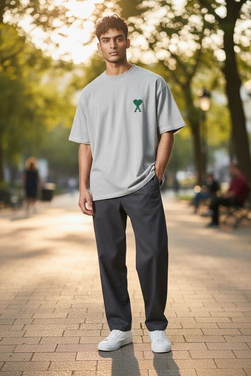 Model wearing an oversized grey AMI Paris t-shirt with a green heart logo at a Parisian cafe.