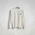 Model wearing a cream Prada crewneck sweatshirt with a green triangle logo on a European street.