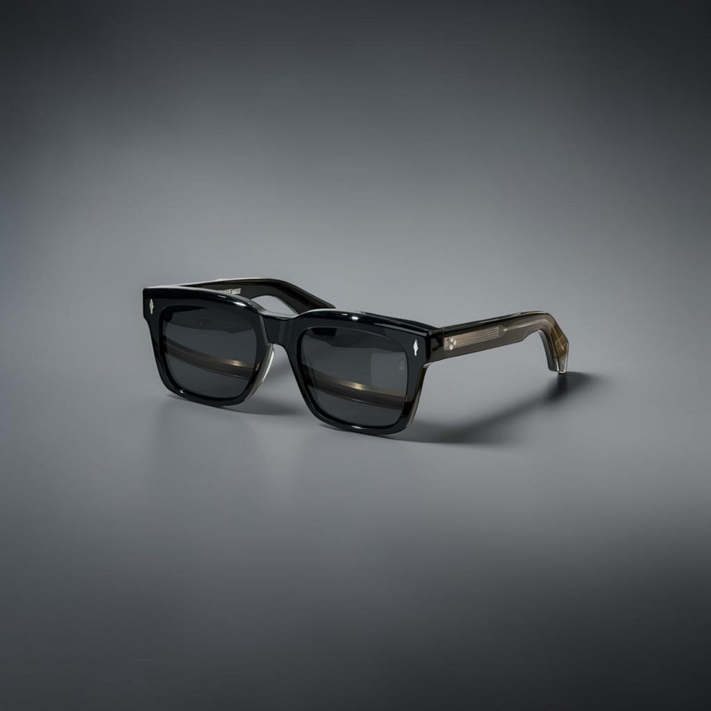 Model wearing thick black Jacques Marie Mage Torino rectangular sunglasses in a city setting.