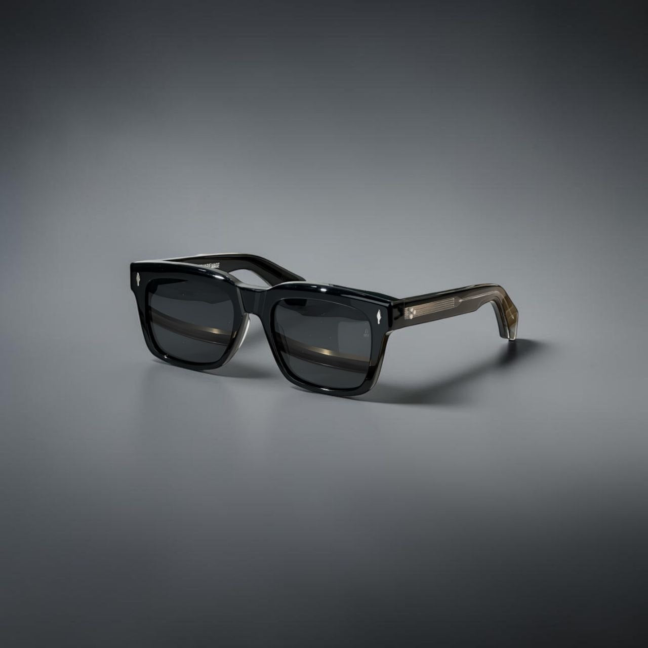 Model wearing thick black Jacques Marie Mage Torino rectangular sunglasses in a city setting.