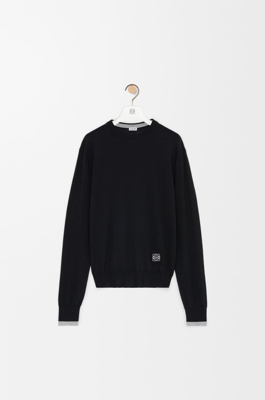 Model wearing a black Loewe wool sweater with a white Anagram logo in a bright, modern cafe"