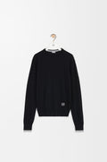 Model wearing a black Loewe wool sweater with a white Anagram logo in a bright, modern cafe"