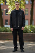 Model wearing a minimalist black Prada cotton t-shirt with a small logo on the chest, styled under a black zip-up jacket.